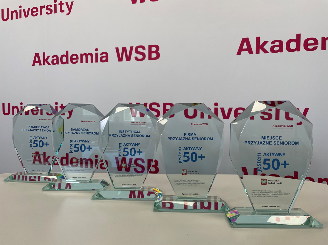 Sześć szklanych statuetek z napisem "Aktywny 50+" na tle logo Akademii WSB.