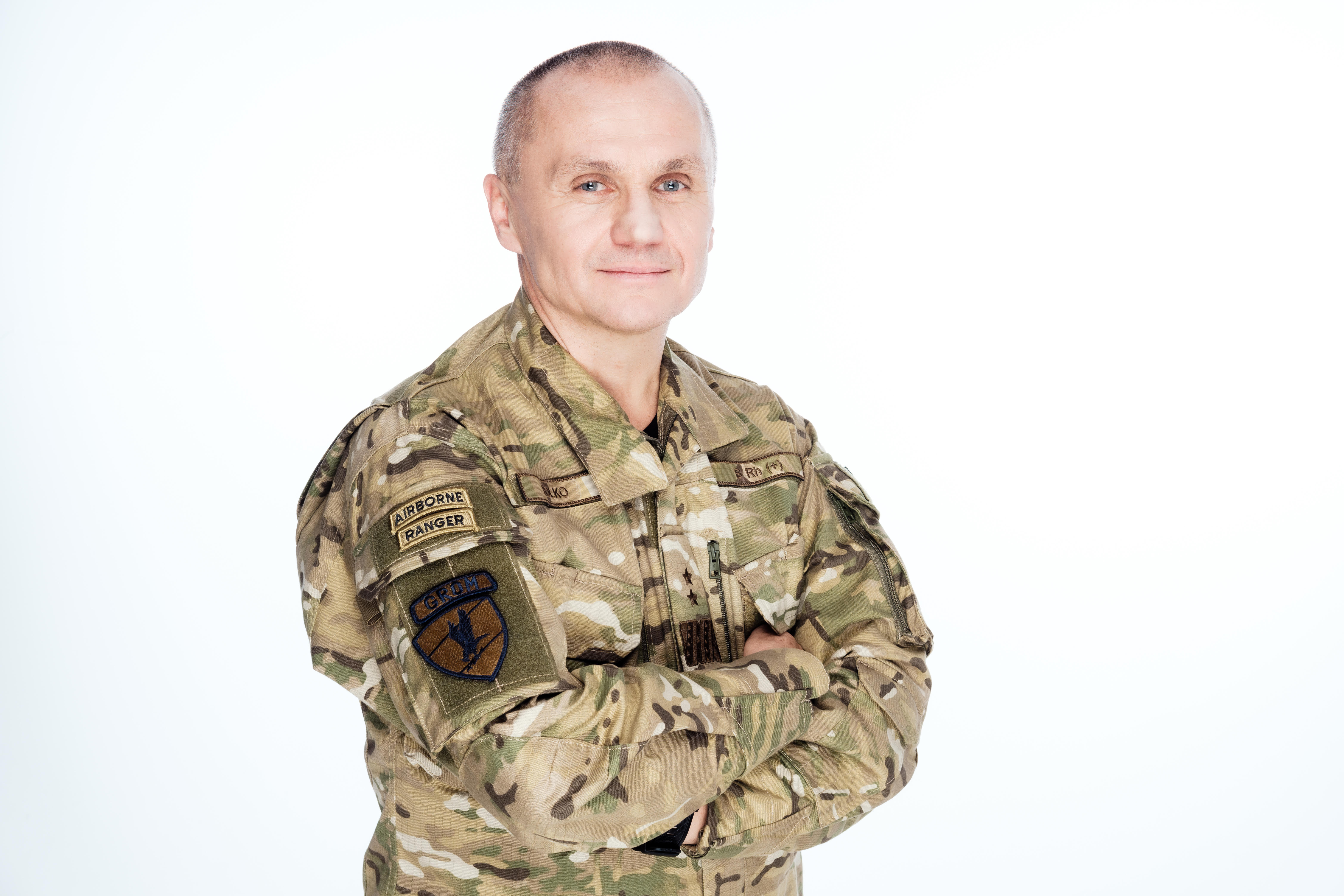 Mężczyzna w mundurze wojskowym z uśmiechem, stojący z założonymi rękami.