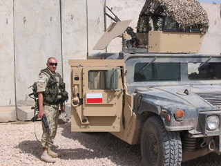 Żołnierz stoi obok opancerzonego pojazdu w terenie pustynnym.