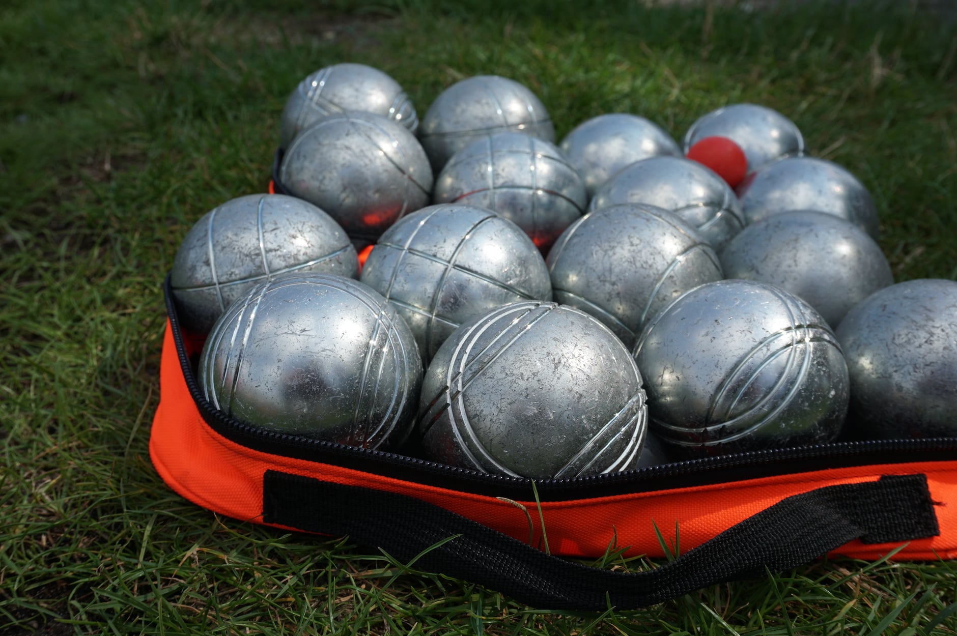 Torba z metalowymi kulami do gry leży na trawie.