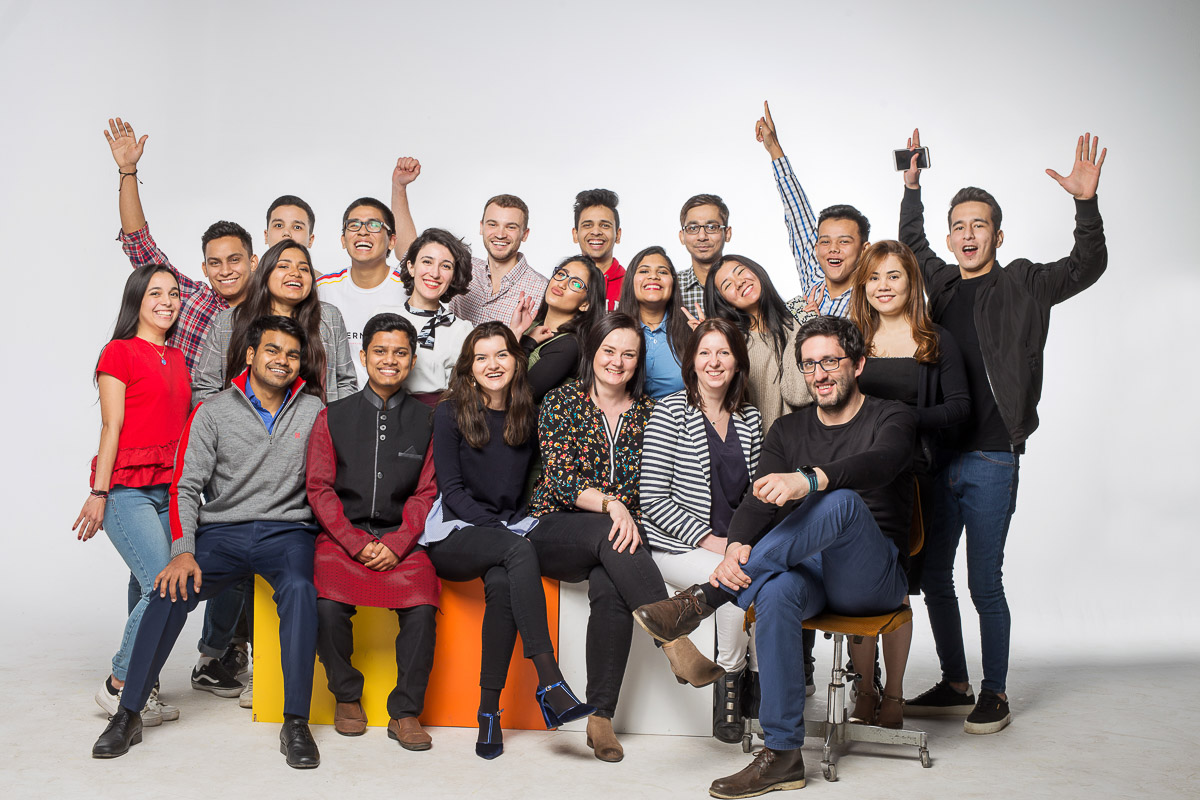 Grupa uśmiechniętych ludzi pozujących w kreatywnej atmosferze na tle jasnej ściany.