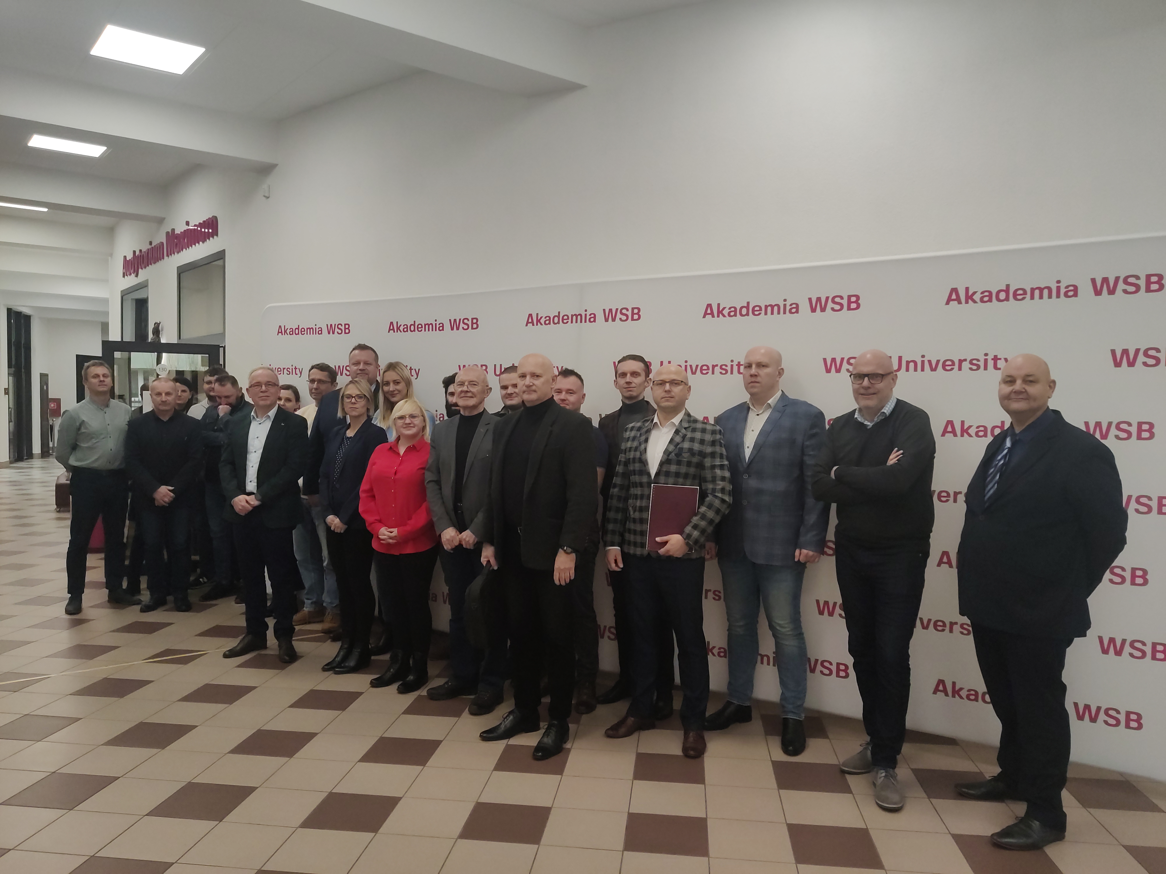 Grupa osób ustawiona w dwóch rzędach przed tłem z logo Akademii WSB.