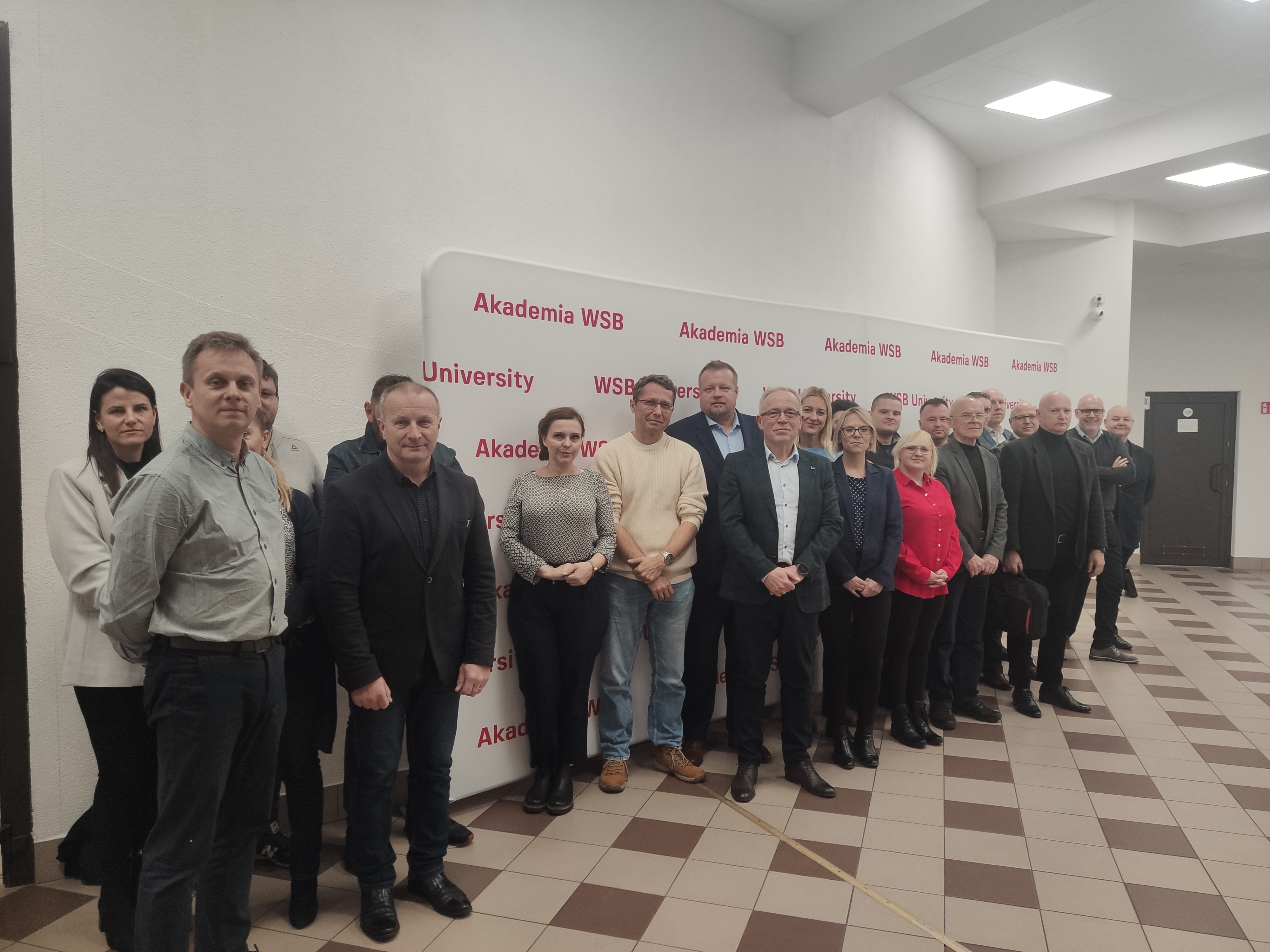 Grupa osób pozująca do zdjęcia przed tłem z logo Akademii WSB.