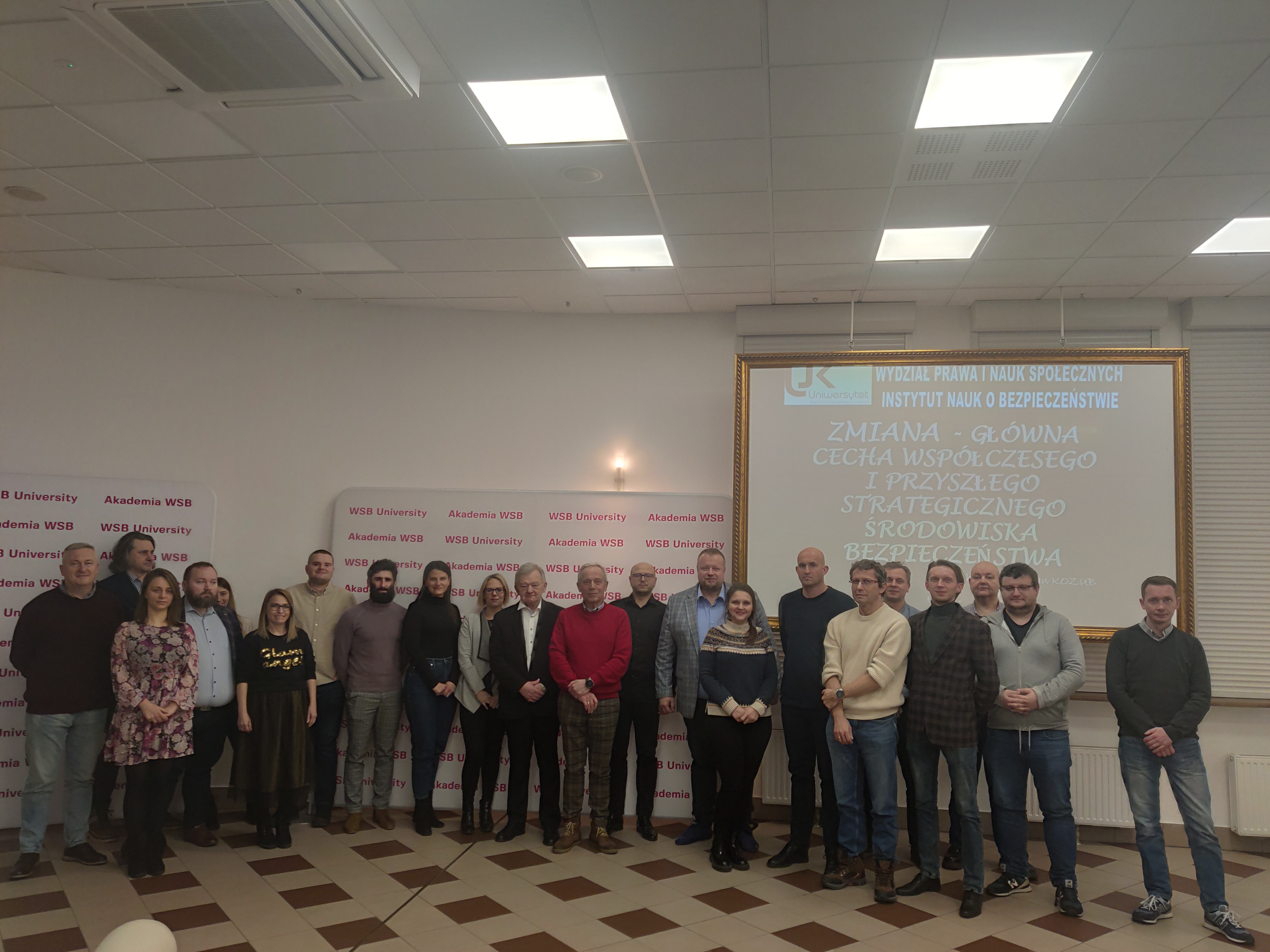 Grupa ludzi pozująca na tle ekranu z prezentacją w instytucie nauk społecznych.